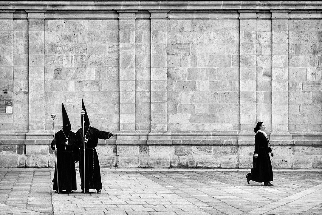 Participantes con túnicas y capirotes junto a un gran muro de piedra.